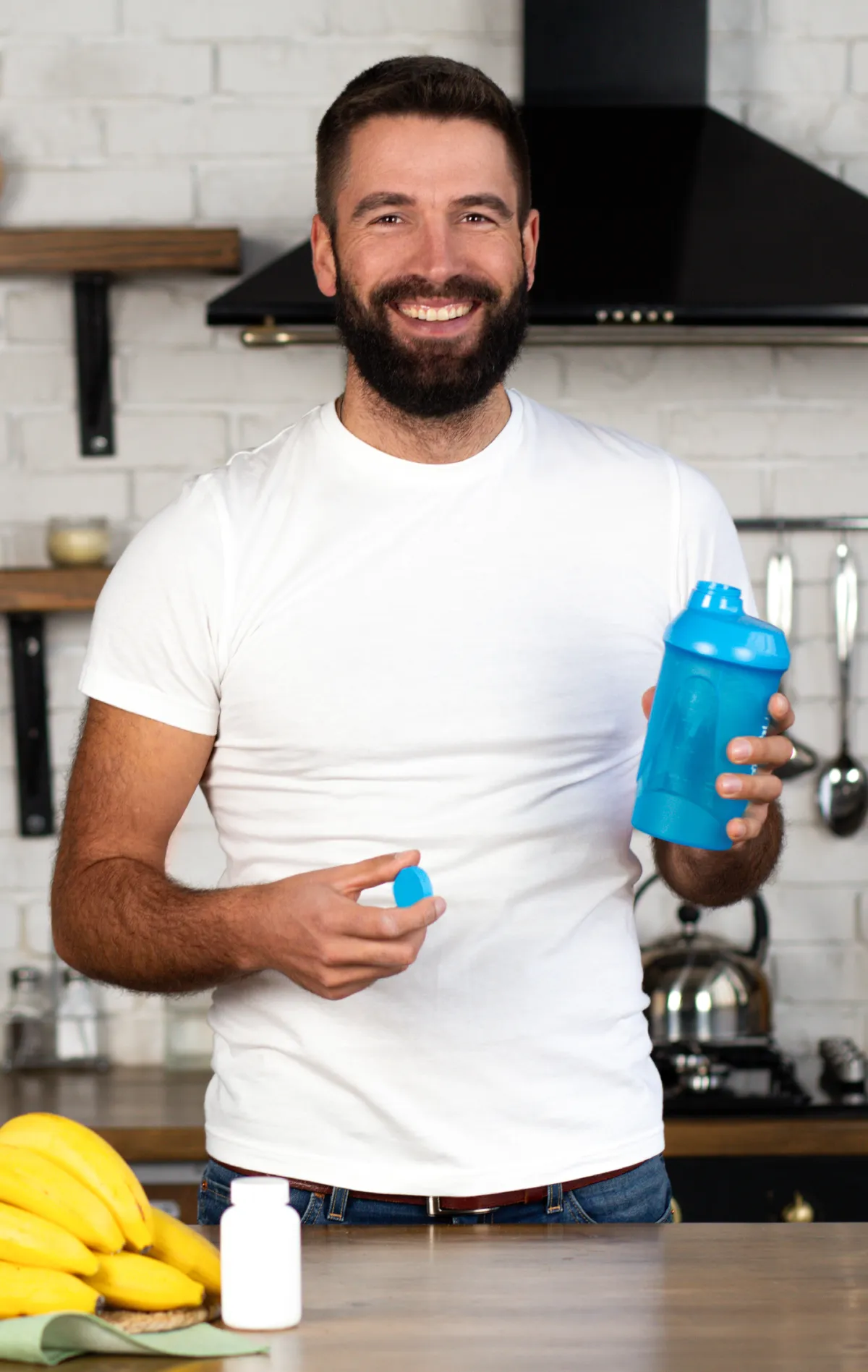 Man smiling in a kitchen in Provo, UT, holding a shaker bottle and a container of supplements, representing targeted nutritional support.